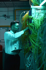 Vertical portrait of handsome data engineer inspecting cables in server room while working with...