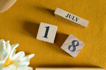 July 18, Wooden Calendar cube on yellow felt fabric with peony flower for date icon background.