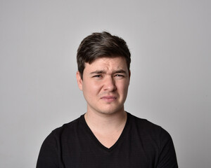 Fototapeta premium Close up head and shoulders portrait of a brunette. young man with a variety of expressive facial expressions. Isolated on a light grey studio background.