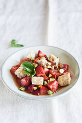 Delicious summer salad. Salad bowl with strawberries, tomatoes, pistachios and croutons in honey orange oil sauce on beige linen tablecloth