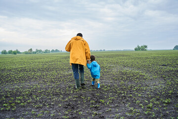 Father and his little son wearing raincoats walking through the swampy field
