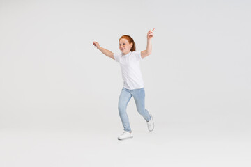 Beautiful cute little red-headed girl in casual outfit running. playing isolated on white studio background. Happy childhood concept. Sunny child