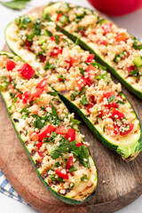 Grilled zucchini stuffed with couscous, tomatoes, cucumber and parsley. Vegan stuffed zucchini on a cutting board. Vegetarian food.