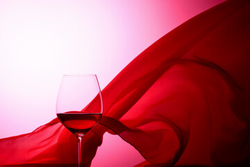Glass of red wine on a background of waving red curtain.