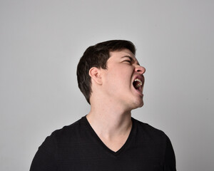 Fototapeta premium Close up head and shoulders portrait of a brunette. young man with a variety of expressive facial expressions. Isolated on a light grey studio background.