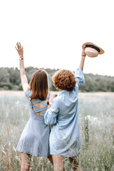 Two young redhead women in blue dresses stand with their backs, hug and enjoy life during the...