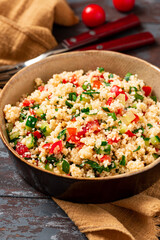 Vegan salad made of couscous, tomatoes, cucumbers, parsley and lemon juice. Couscous with vegetables in a bowl on a dark wooden background. Tabbouleh salad.