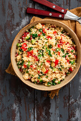 Vegan salad made of couscous, tomatoes, cucumbers, parsley and lemon juice. Couscous with vegetables in a bowl on a dark wooden background. Tabbouleh salad.