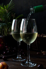 White wine is poured into glasses. There are fruits nearby