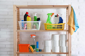 Shelving unit with detergents and toilet paper near white brick wall