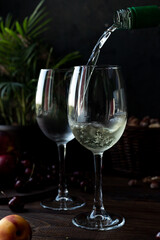 White wine is poured into glasses. There are fruits nearby