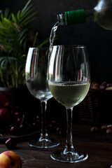 White wine is poured into glasses. There are fruits nearby