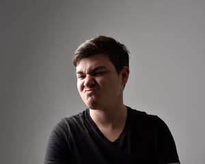 Close up head and shoulders portrait of a brunette. young man with a variety of expressive facial expressions. Isolated on a light grey studio background.