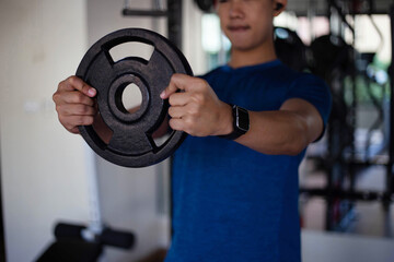 Fototapeta na wymiar Training gym concept a muscled male teenager using both hands holding a heavy iron wheel