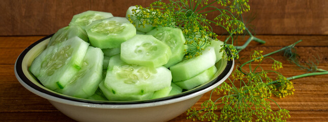 Juicy raw cucumber salad in a plate on a wooden table with dill