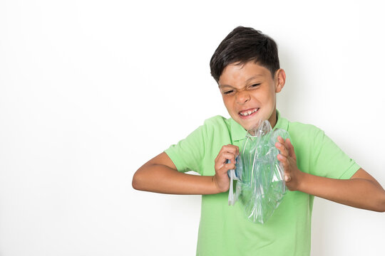 A boy makes gestures of strength while crushing a plastic bottle with his hands to recycle it. Recycling concept for children