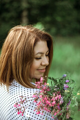 Naklejka premium A girl with a short haircut laughs and holds flowers in her hands. A close portrait from the back of a young beautiful woman in a meadow with a bouquet of lilac wildflowers. Selective focus