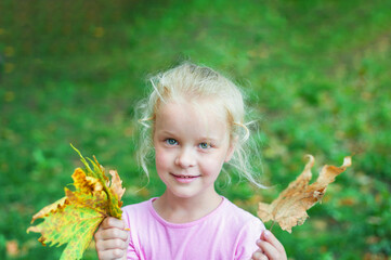 portrait of a happy little girl holding a bouquet of autumn leaves in her hands