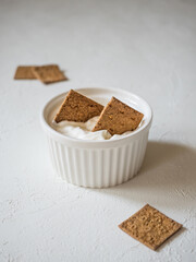 Flat natural mini crunchy bread in a gravy boat with sour cream. Dip the crunchy breads in the sauce. Delicious and natural dietary snacks.