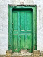 Old door in an intense water green color with the number 7. Vintage door with texture. Door from an old house in the north of Spain