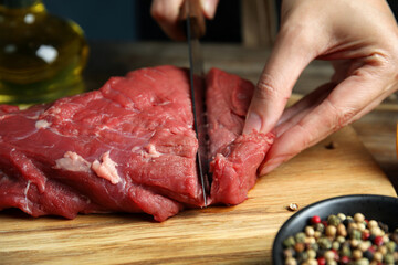 Woman cutting fresh raw meat at wooden table, closeup