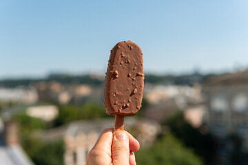Tasty black ice cream with caramel pieces on a stick in hand