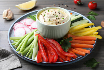 Fresh raw vegetable sticks and sauce on grey wooden table, closeup