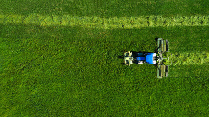 Aerial view of a tractor mowing a green field with fresh grass. Tractor cleaning of excess grass...