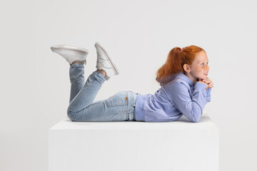 Side view. Portrait of smiling red-headed girl in casual clothes isolated on white studio...