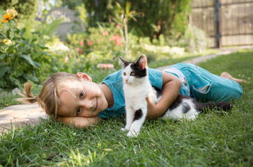 kid plays outdoors in the summer with his beloved black and white kitten. the child is friendly with the pet. Toddler boy lies on the grass with the cat. Holidays in pleasure, joy, positive