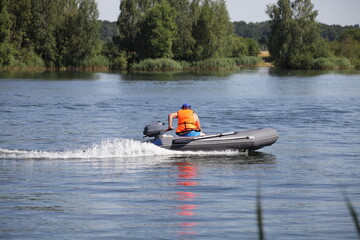 One man in orange lifejacket fast floating on inflatable motor boat with small outboard motor on...