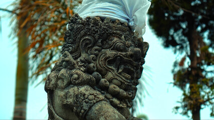 old Indonesian ethnic stone statue of an evil demon with an open mouth and fangs covered with cloth