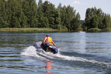 Moving away inflatable motor boat with outboard motor and  man in orange lifejacket fast floating...