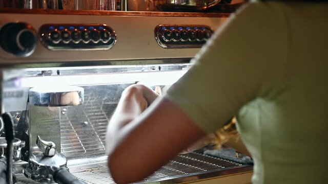 Asian female barista making hot coffee with bottomless portafilter and pressing button of coffee machine in coffee shop