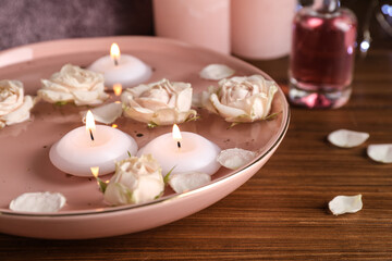 Bowl with water, burning candles and roses on wooden table, closeup. Space for text