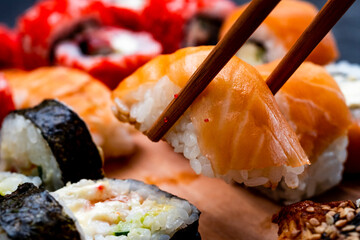 Closeup view on set with sushi, maki and sashimi with raw fish salmon. Person picks up traditional japanese roll with wooden chopstick. Oriental asian food