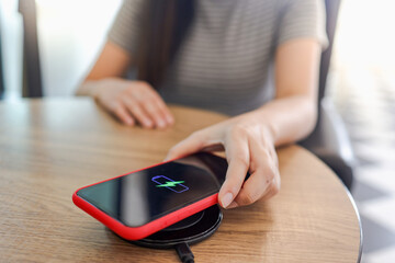 Fototapeta premium Charging mobile phone battery with wireless device in the table. Smartphone charging on a charging pad. Mobile phone near wireless charger.