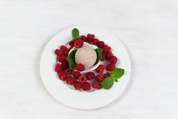 Bowl with raspberry ice cream, mint leaves and fresh ripe berries on white table
