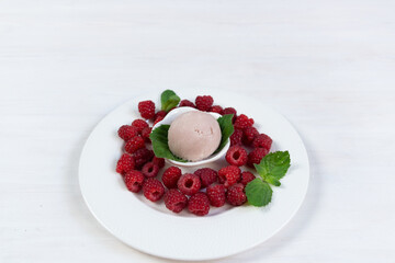 Bowl with raspberry ice cream, mint leaves and fresh ripe berries on white table