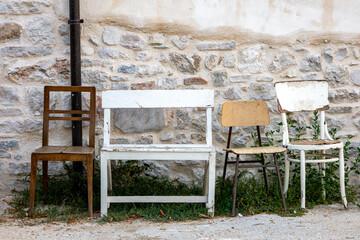 Row of vintage wooden chairs in front of an old stone building, lined up next to a petanque field for players to rest.
