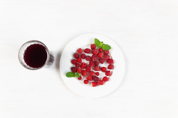 Ripe red raspberries on white plate an glass of juice