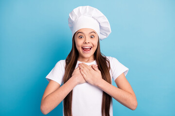 Photo of amazed astonished happy small lady hold hands chest gift wear hat chef isolated on blue color background