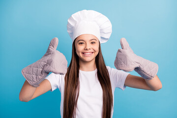 Photo of cheerful positive happy little lady wear chef hat gloves make thumbs-up isolated on blue...