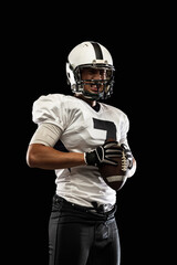 Portrait young American football player, athlete in black white sports uniform posing isolated on dark studio background. Concept of professional sport, championship, competition.