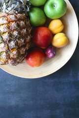 Wooden bowl with various colorful fruit on dark background. Top view.