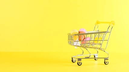 Shopping cart with ice cream inside on a yellow background, closeup. Black Friday Shopping and Discount Concept.