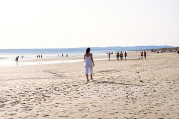 Fototapeta na wymiar Chica joven vestida de blanco caminando sola por la orilla de playa al atardecer