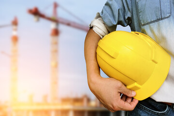 Hand's engineer worker holding yellow safety helmet with building on construction site background
