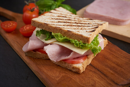 Sandwich with ham and cheese. Grilled and pressed toast with smoked ham, cheese, tomato and lettuce served on wooden cutting board. Cafe - Sandwich with bacon, cheese, ham and vegetables.