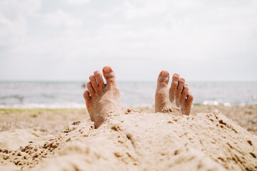 Male feet in sand on beach. Sunbathing, summer vacation, tan concept. Happy tourist rests near sea or ocean.
